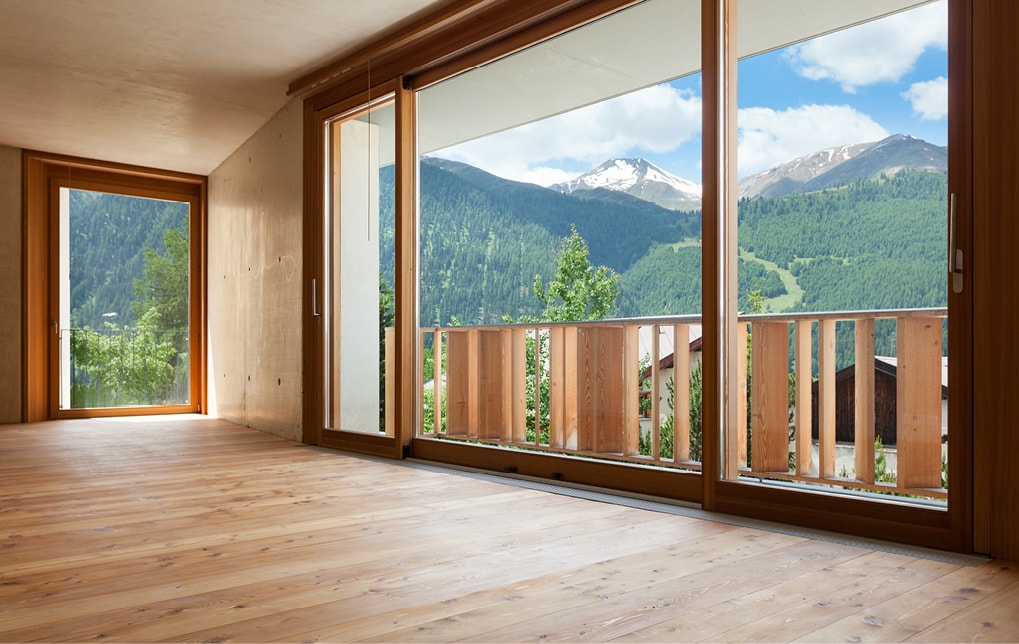 Blick auf Berglandschaft durch großflächiges Strussnig-Holzfenster in leerem Raum mit Parkettboden