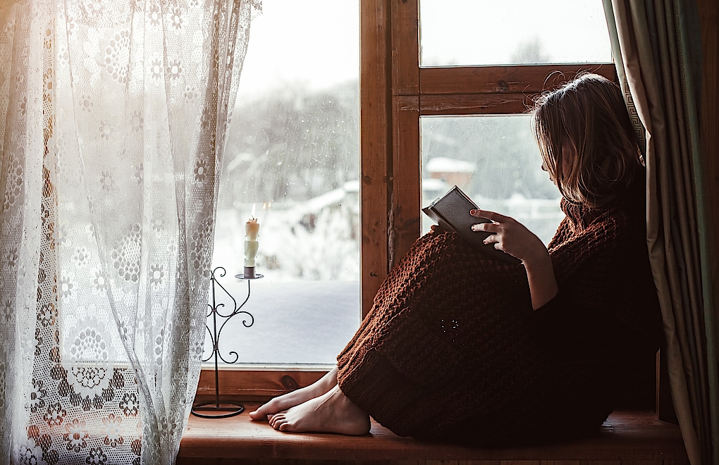 Lesende Frau vor Holzfenster mit Blick auf Winterlandschaft