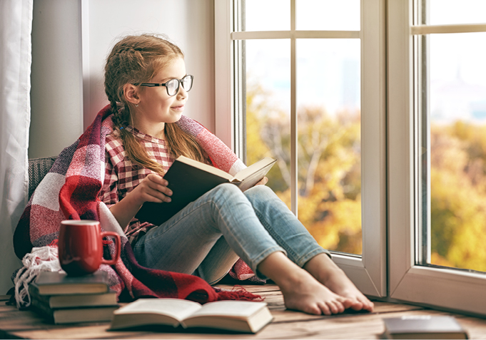 Kind mit Buch in der Hand blickt aus Fenster